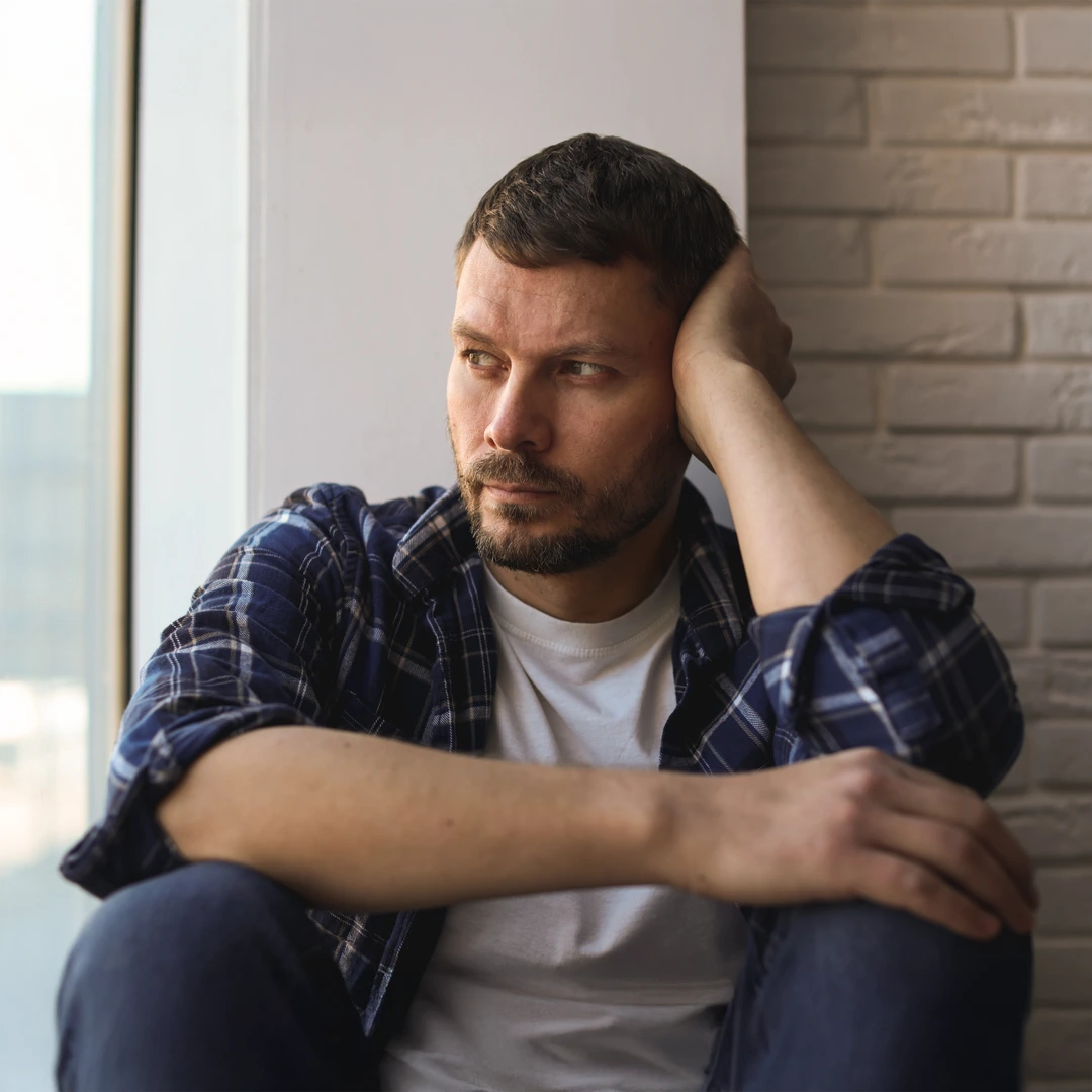 Thoughtful man sitting against a brick wall, reflecting on the challenges of alcohol addiction, symbolizing the need for compassionate rehab treatment in Phoenix.