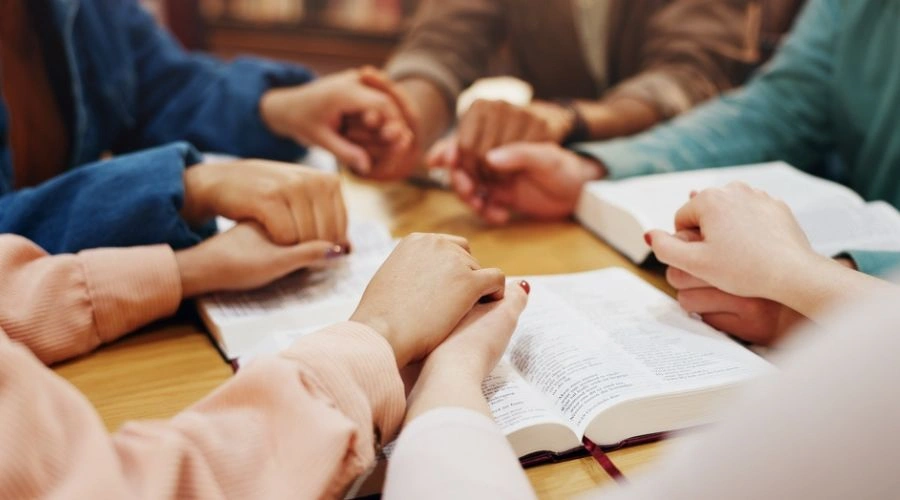 Group sitting with holding hands next to each other and reading from the bible