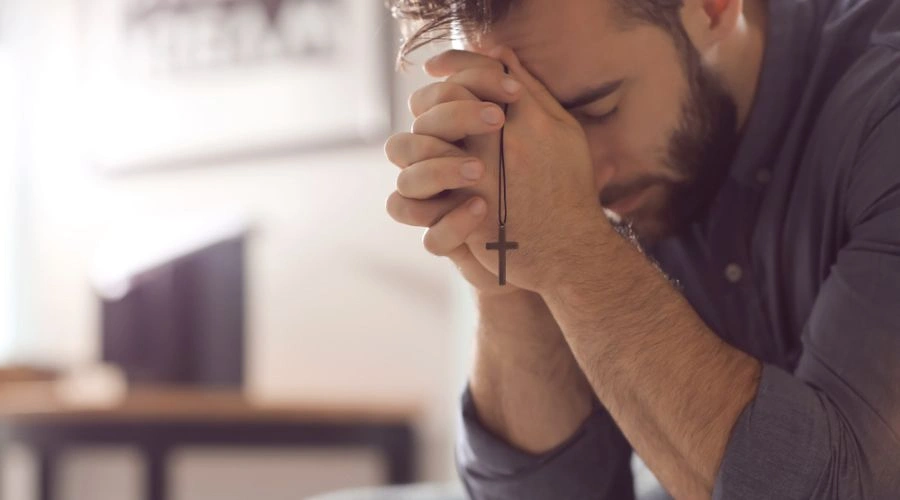 Man with eyes closed holding a cross and saying his Personal Prayer