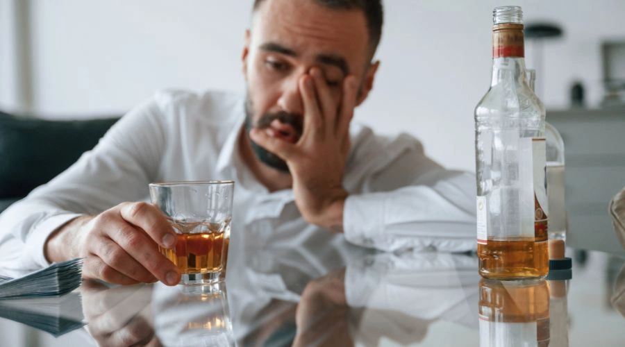 Distraught man with almost empty bottle of liquor ready to drink another glass of liquor
