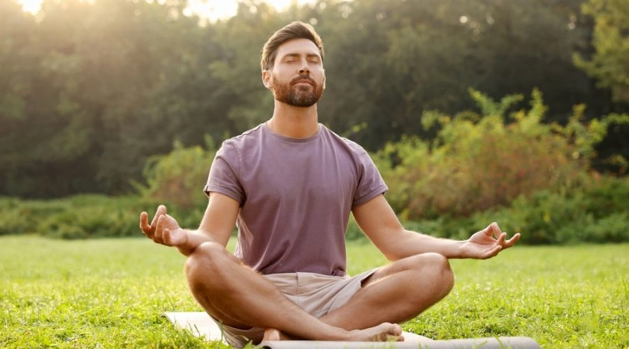 Man sitting on the grass outside, meditating to a higher power in a yoga position.