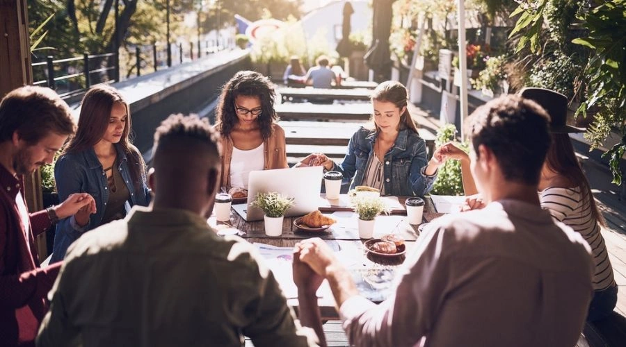 Group members siting at a table with hands joined reciting the Serenity Prayer