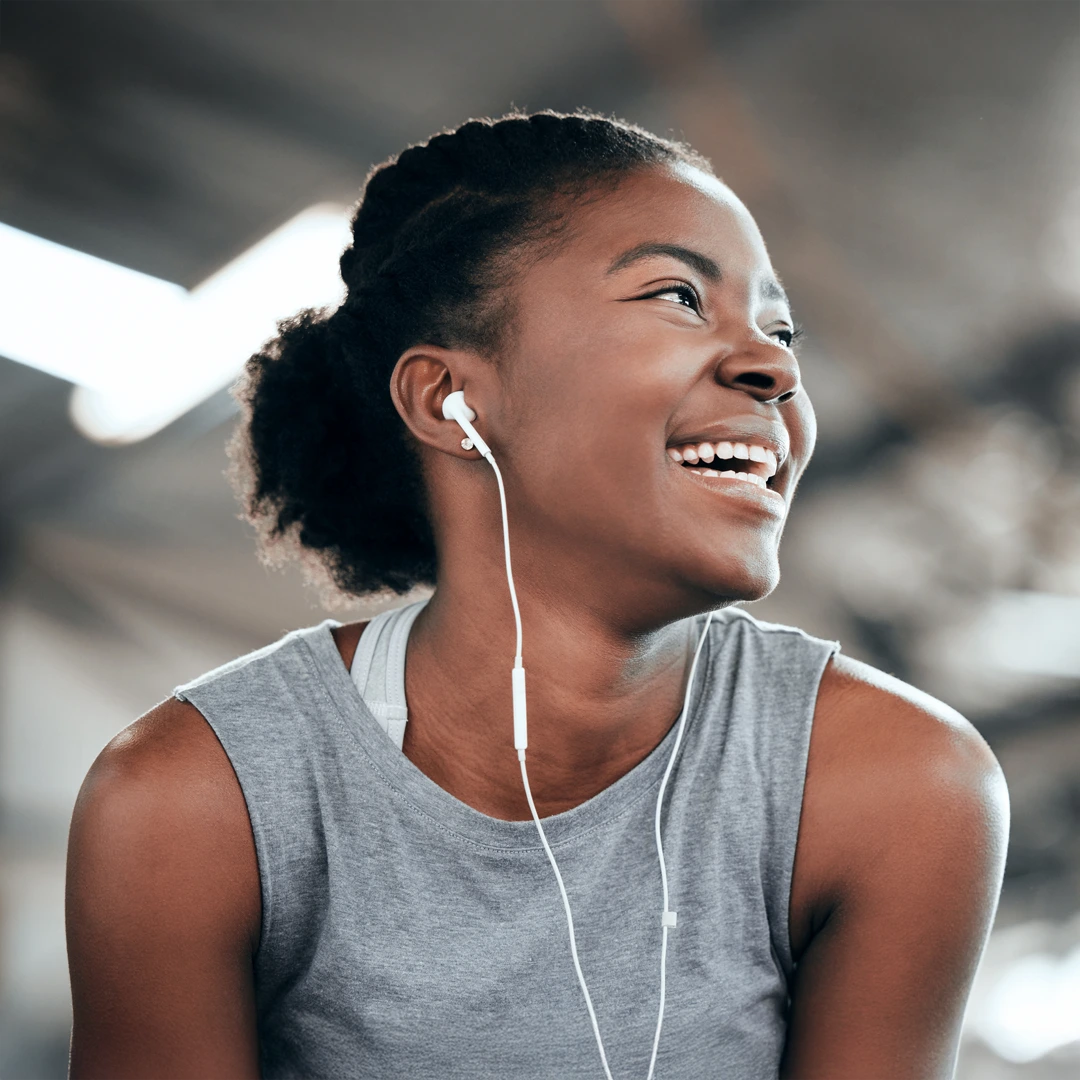 Joyful young woman in an athletic top wearing earbuds, looking to the side and laughing—symbolizing hope and Mercy Care–covered comprehensive drug and alcohol treatment at Changes Healing Center in Arizona.