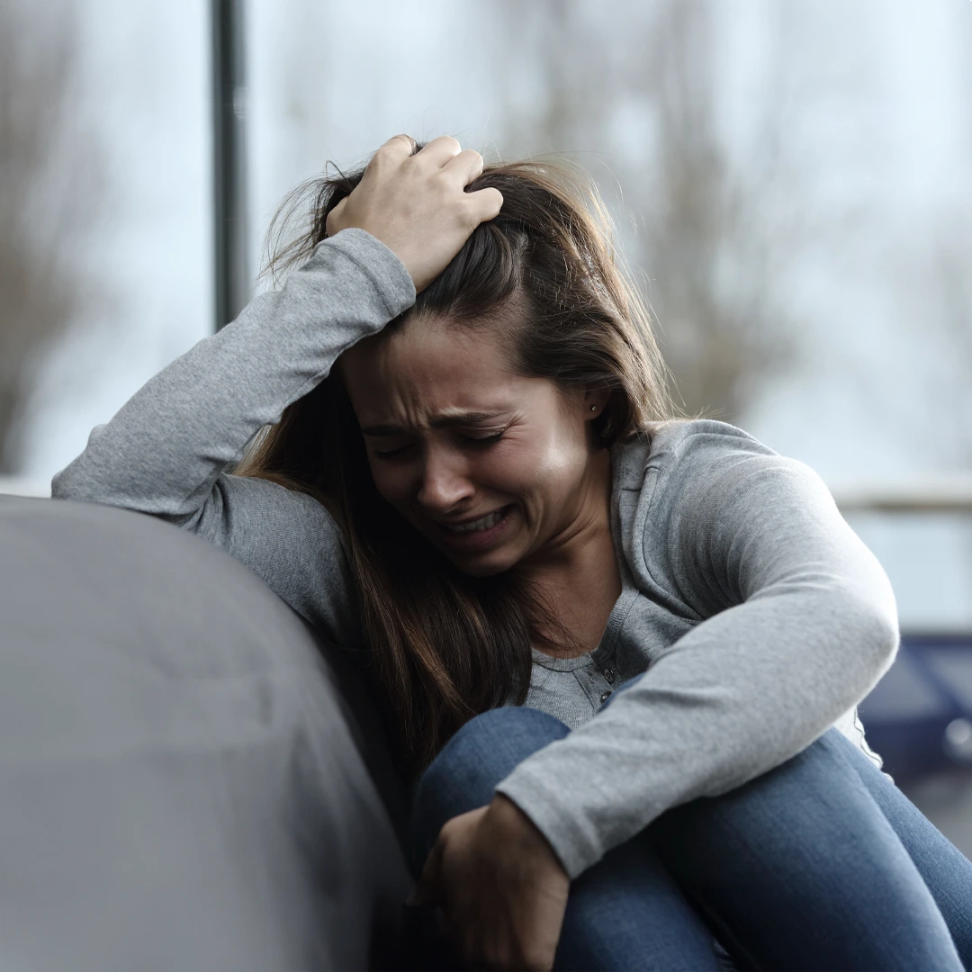 Crying woman leaning against a couch, overwhelmed by the struggles of alcohol addiction, representing the urgent need for supportive rehab treatment in Phoenix.