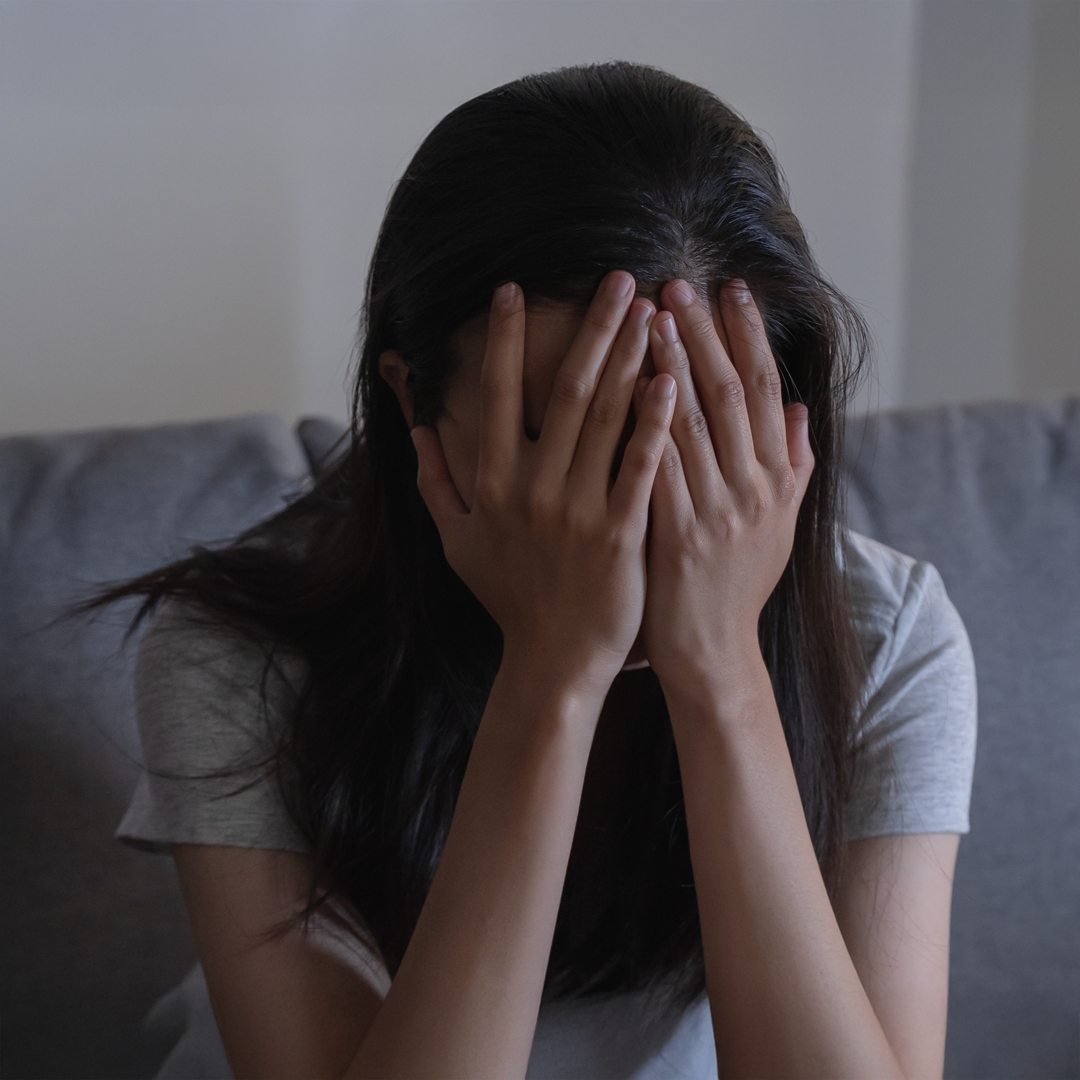 A distressed woman sits on a couch with her face buried in her hands, symbolizing the emotional toll of addiction and the urgent need for compassionate support.