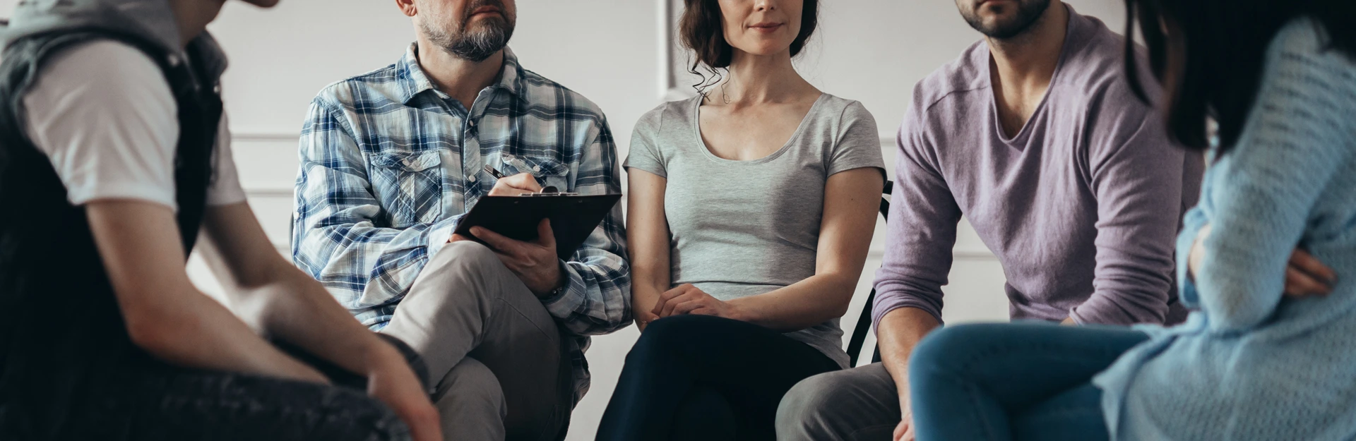 Adults seated in a circle during group therapy, therapist taking notes, reflecting compassionate care at Changes Healing Center.