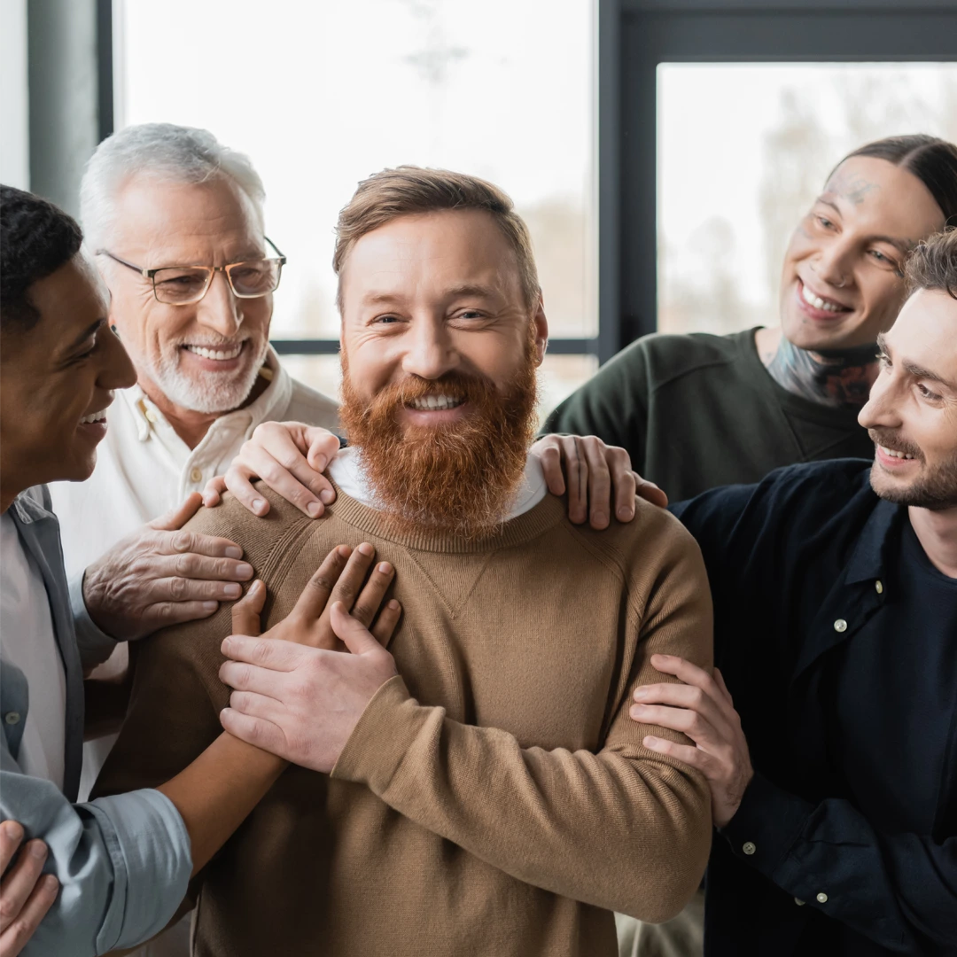 Men smiling with supportive hands on shoulders—peer community in residential treatment.