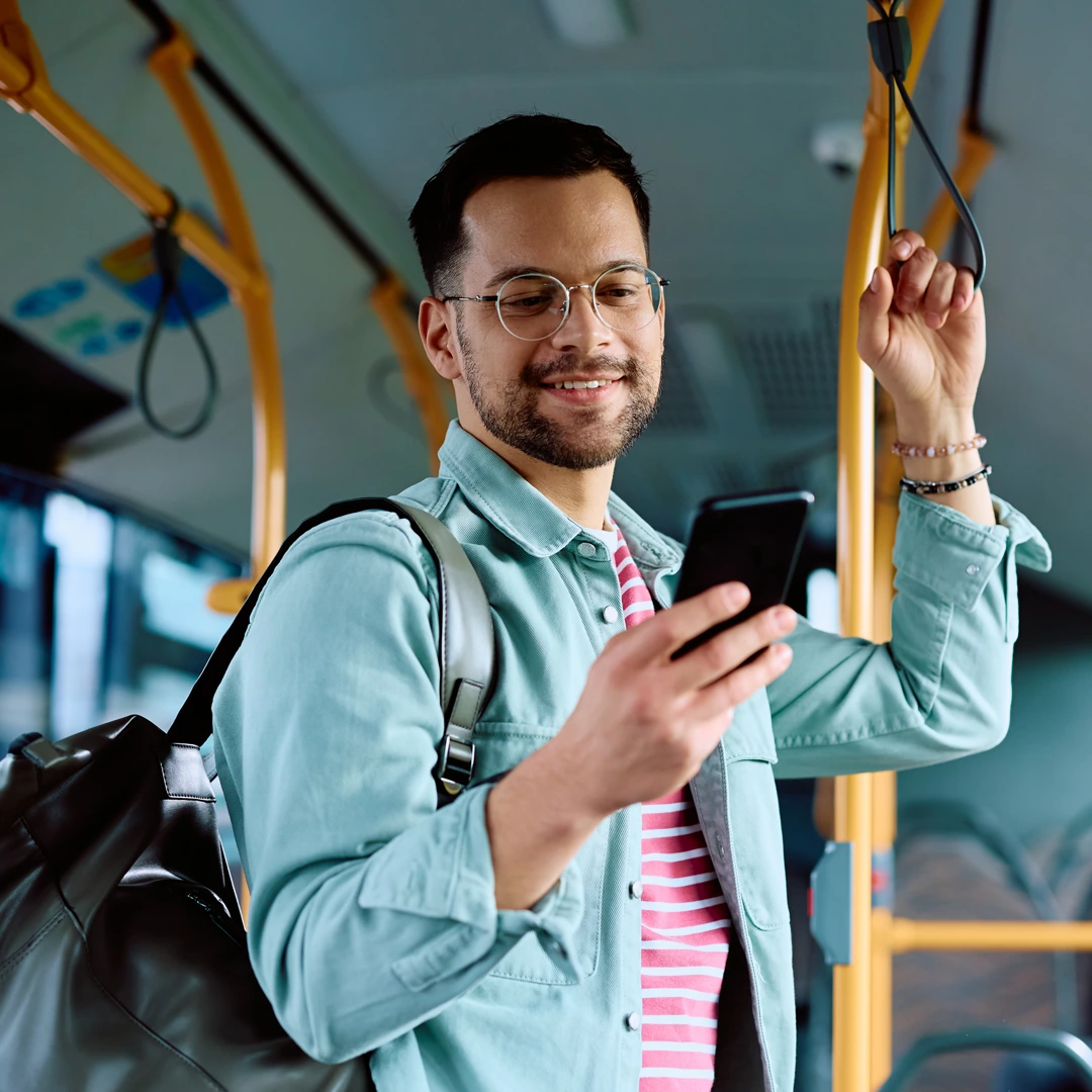 Young man with glasses holding a phone and smiling while riding a bus, symbolizing balance, independence, and recovery from marijuana addiction.