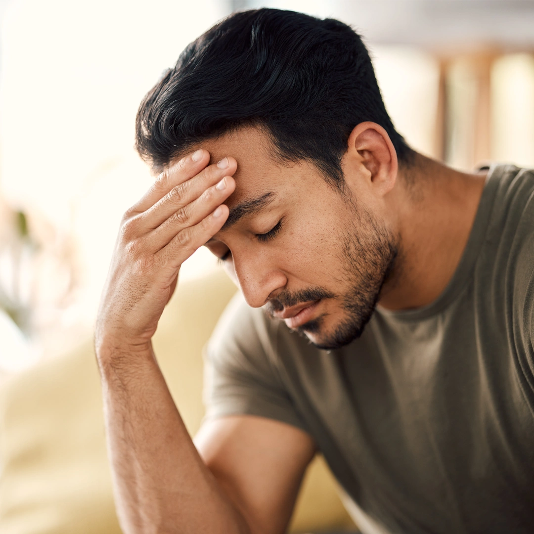 Man sitting with eyes closed and hand on forehead, showing emotional distress and the weight of unresolved trauma.